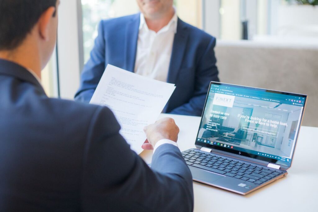 back of josh de buelle at desk holding a home loan document, in front of open laptop